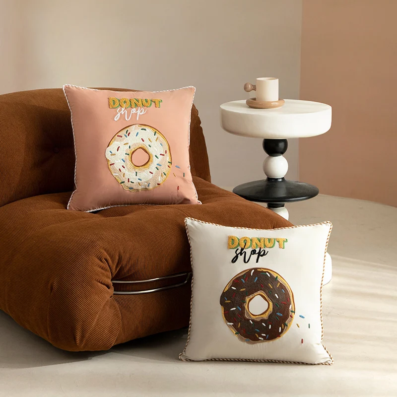 Quadratisches Dekokissen mit gesticktem Donut-Motiv und dekorativer Kederkante